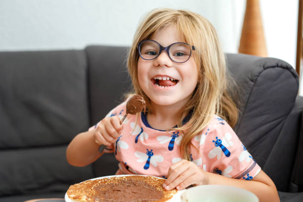 Adorable little girl having breakfast, eating pancakes with chocolate cream. Preschool child smiling. Sweet food for children. stock photo