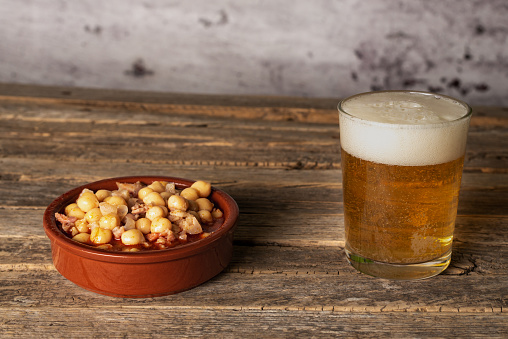 Clay plate with tripe and chickpeas, next to a glass of beer, on an old wooden table.