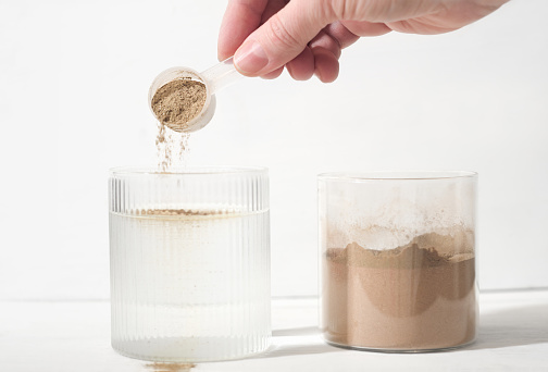 woman pouring plant based protein powder into a glass of water. plant protein as food supplement, bones and joints health support