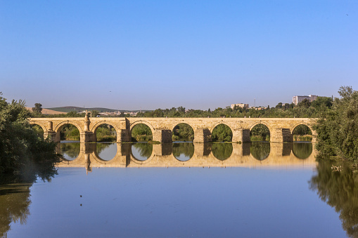 Cordoba, Spain - May 26. 2022: Ancient roman bridge across the Guadalquivir river in the morning tranquility at the medieval city of Cordoba, Andalusia. Spain
