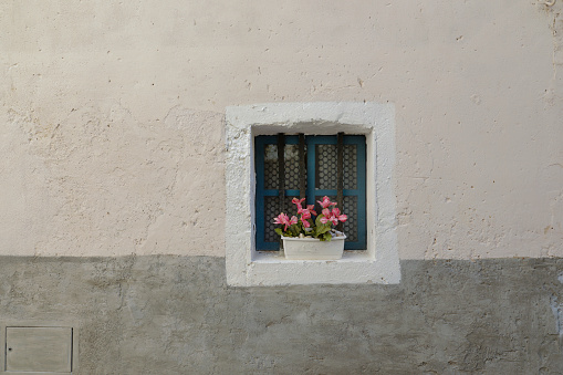 Stone house wall bright and grey with small window and flowers of the windowsill