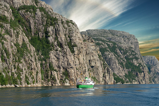 Norway, Lysefjord  - Sep 7, 2022:. Vessel in picturesque rock mountain fjords landscape sunset sea view.