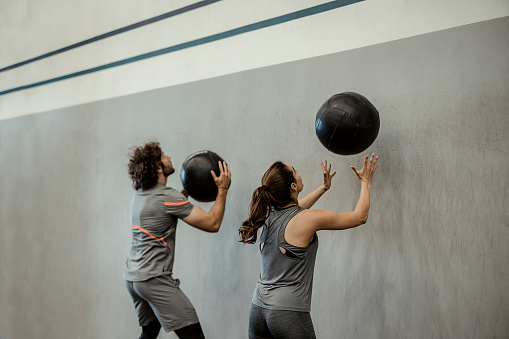 Fit man and sporty woman doing exercise together using medicine ball in gym