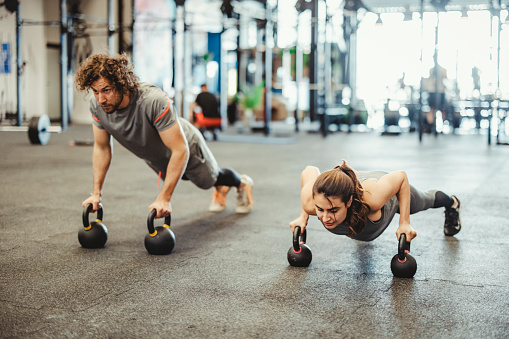 Two sporty young people exercising pushups on kettlebell at functional fitness gym