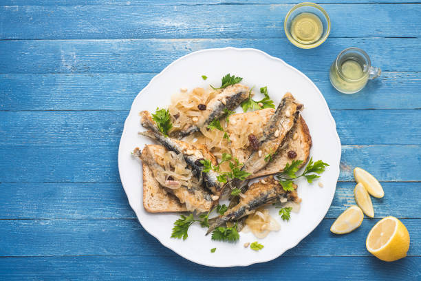 Marinated  sardines or Sarde in saor, a typical dish from the Venice, Italy  with white onions marinated with wine vinegar, raisins and pine nuts, served with bread. Blue marine wooden table. Copy space