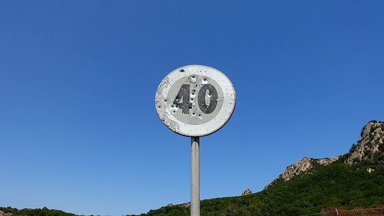An old road sign on a mountain road indicating the speed limit, perhaps riddled with rifle shots.