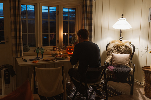 Silhouette of a male sitting at the table with window view of the mountains having dinner with candles and Jack O'Lantern during Halloween night