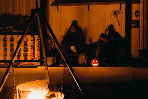 A couple sitting by the campfire with Jack O'Lantern lighting at the terrace outdoors in Norway