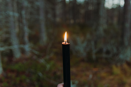 Female walking in the spooky woodland during the dark evening time holding candle in Norway