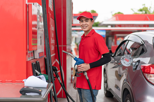 Young man worker in red uniform holding fuel pump nozzle refuel at gas station