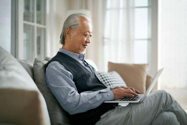 istock elderly asian man sitting on couch looking at notebook computer 1444701905