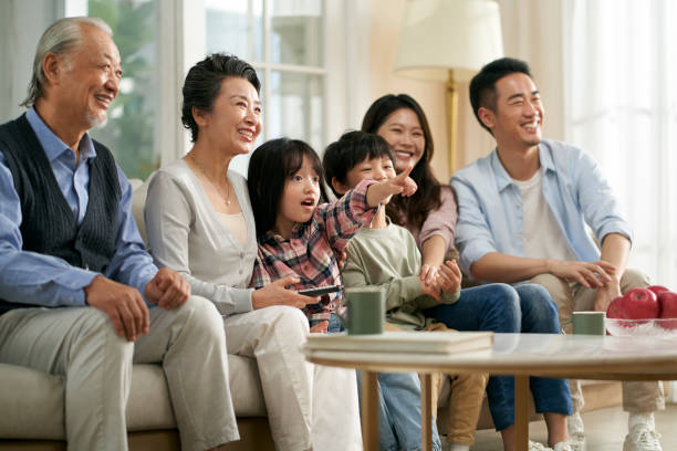 three generation asian family watching tv together at home three generation asian family sitting on couch at home watching tv together happy and smiling china chinese ethnicity smiling grandparent stock pictures, royalty-free photos & images