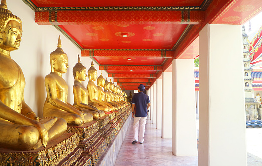 Visitor Admiring the Row of Sitting Postured Buddha Images at the Cloister Called Phra Rabiang of Temple of the Reclining Buddha, Bangkok, Thailand