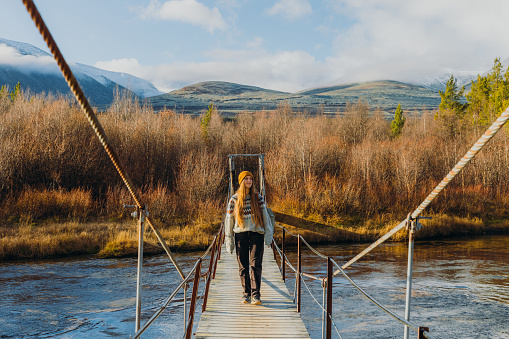 Female backpacker hiking on the wooden bridge above the river steam in the mountains of Norway overlooking the sunny golden bright mountain landscape