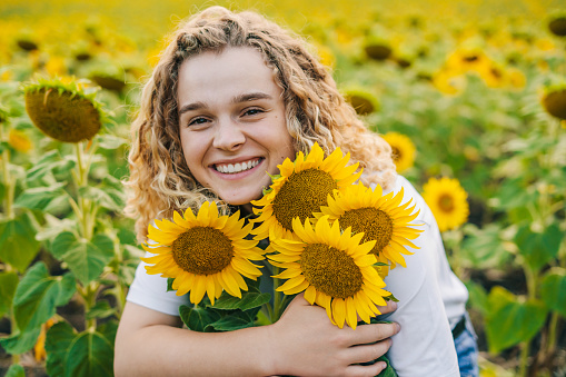 Lovely cheerful young woman rejoicing and enjoying sunflower field blooming on a summer day. People lifestyle. Nature summer. Beauty portrait.