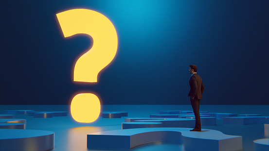 Concepts of making the right decisions and answering the right questions. Man stands in  front of a giant illuminated question mark. He stands on question marks on the floor.