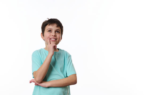 Happy child boy olding his hand at chin and cutely smiling, thoughtfully looking aside, isolated over white backdrop stock photo