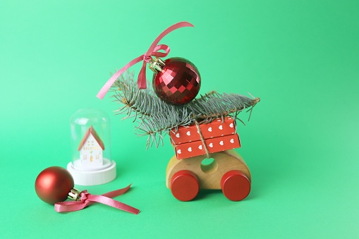 Christmas, a toy car with wrapped gifts and spruce branches, a red ball with a bow, a toy house on a green background, the concept of congratulations, a postcard