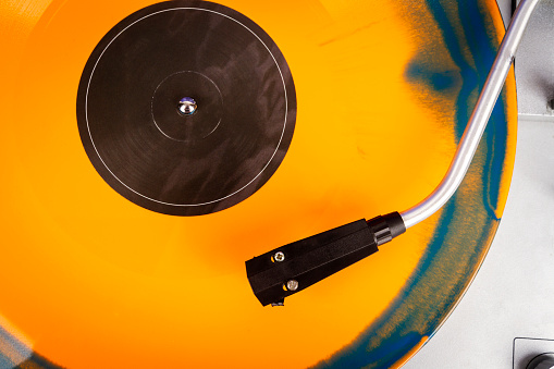 Close up of turntable needle on a vinyl record. Turntable playing vinyl. Needle on rotating orange and blue vinyl.