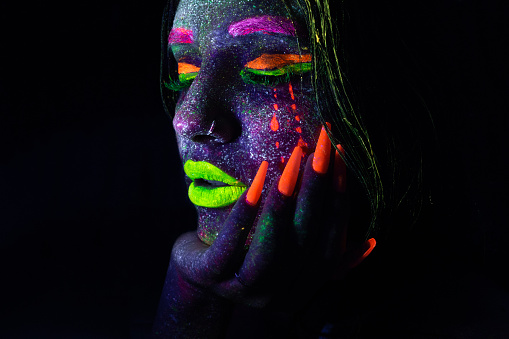 Portrait of young girl under ultraviolet light neon makeup on her face