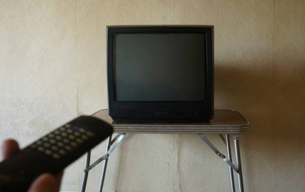 istock Watching TV. Person hand using tv remote controller. Old vintage television with noise interference on the screen. Male hand holding TV remote control. changing channels. television, channels surfing 1444727670
