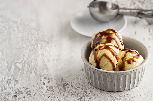 Vanilla ice cream  with caramel into the ceramic bowl on light background . Copy space
