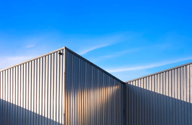 гофрированная стальная стена складского здания на фоне голубого неба с солнечным светом и тенью на поверхности - corrugated iron стоковые фото и изображения