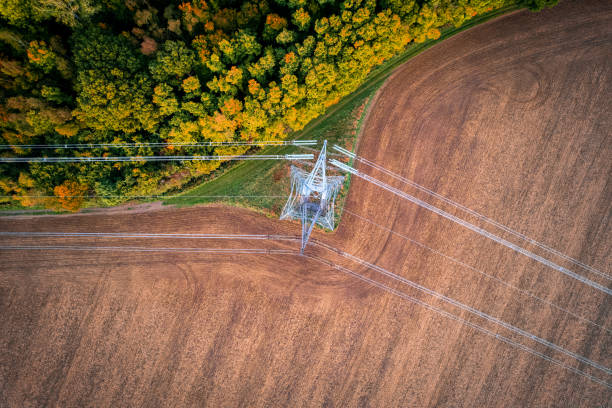 Electricity line changing direction 400kV extra high voltage electricity line changing direction above cultivated field contracting with autumn forest, shot from above with drone. power cable stock pictures, royalty-free photos & images