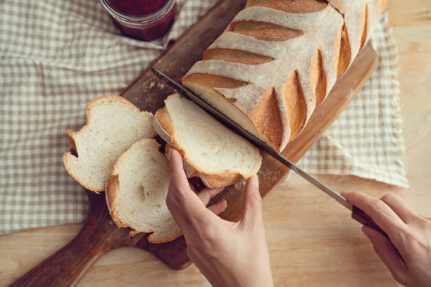 istock Female hands cutting crusty bread loaf on a wooden board 1444741277