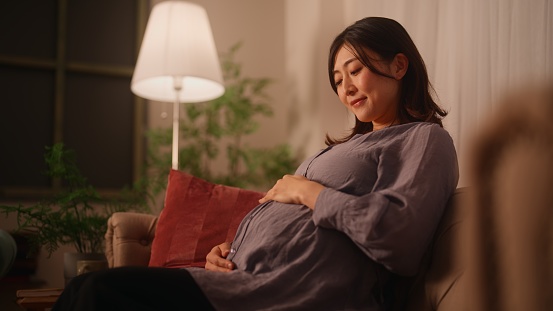 A pregnant woman is sitting on a sofa resting and relaxing in the living room at home.