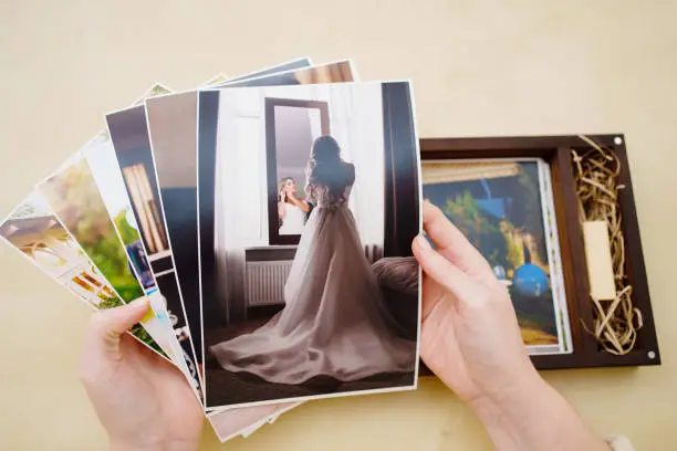 Photo of printed wedding photos in the hands and in a wooden box with a flash drive.