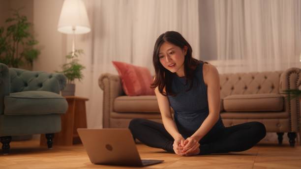 istock Pregnant woman sitting on floor and stretching her body while watching online tutorials on laptop in living room at home 1444745356