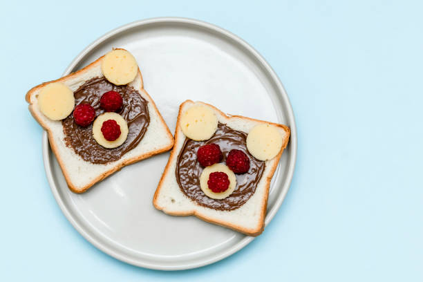 istock Funny bear face sandwich toast bread with peanut butter, cheese and raspberry on plate blue background. Kids child sweet dessert breakfast lunch food close up 1444752651