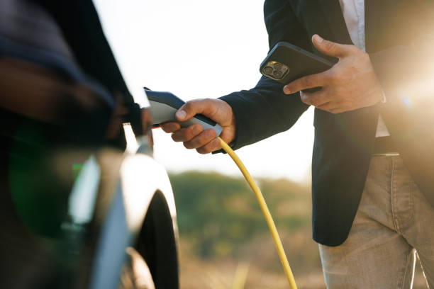 istock Male charging EV vehicle outdoors at sun light. Businessman unplugging zero emission electric car at charging station. Man disconnects charging cable to to electric vehicle using app on smartphone 1444753864