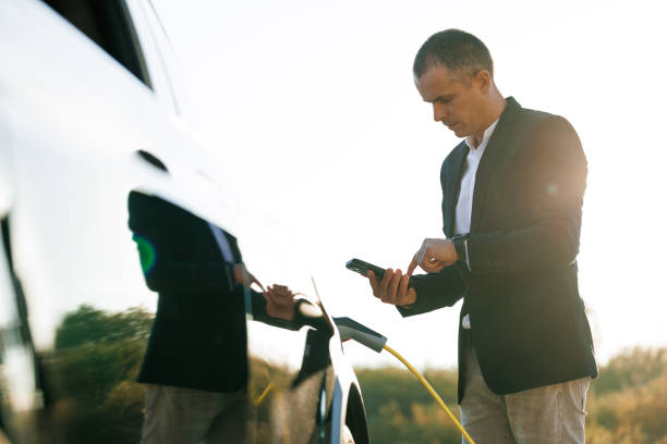 istock Male charging EV vehicle outdoors at sun light. Businessman unplugging zero emission electric car at charging station. Man disconnects charging cable to to electric vehicle using app on smartphone 1444753869