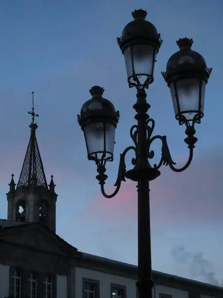 Church bell tower, townsquare, old-fashioned street light at dusk. Lugo city, Galicia, Spain.