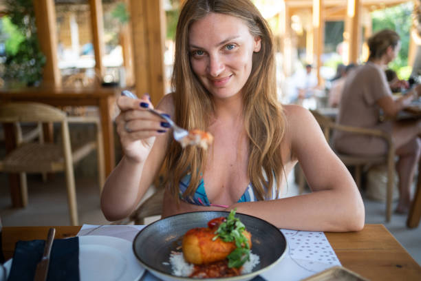 istock A woman in a restaurant eats fried chicken meat with rice, sauce and arugula, looking at camera 1444760265