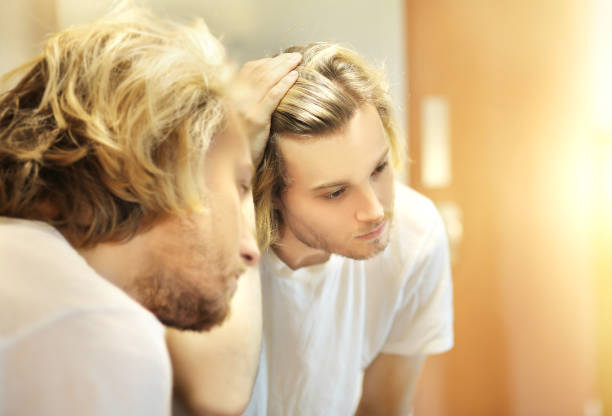 istock young man looking in the mirror,combing his hair,looking at problems on face. 1444761842