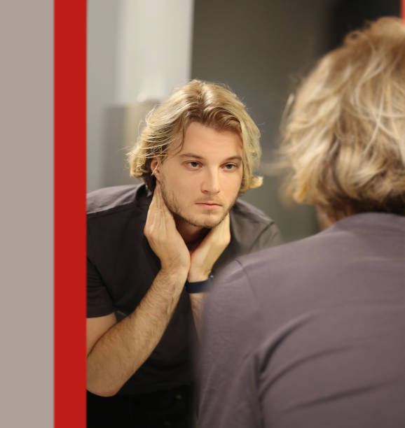 istock young man looking in the mirror,combing his hair,looking at problems on face 1444762001