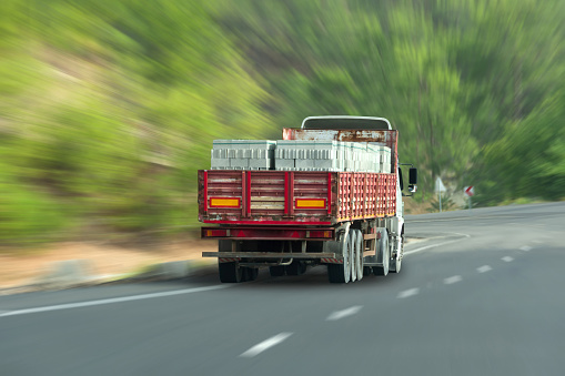Truck with a trailer and foam blocks loaded into it, a building material, drives along a highway in the middle of a forest with the effect of speed motion blur