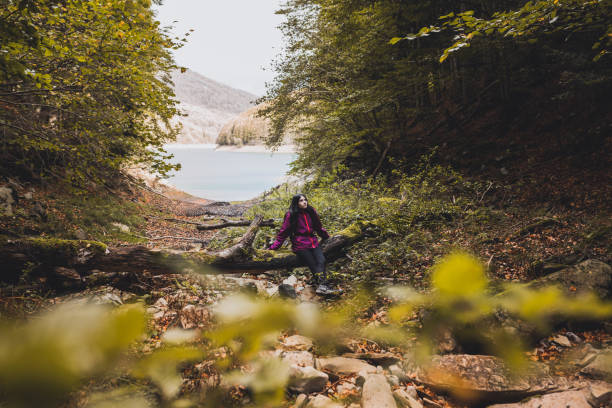 istock Happy girl resting on a fallen beech tree while hiking through the Irati forest (Navarre, Spain) in Autumn. 1444765326