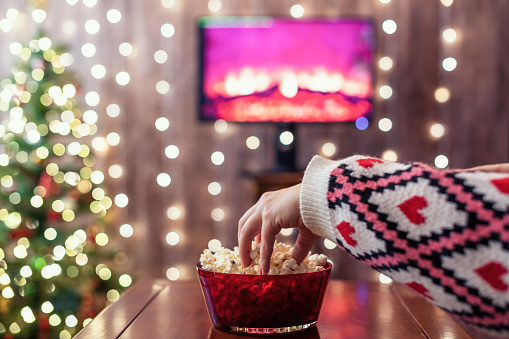 Christmas eve. Alone woman watching tv and eating popcorn. Home cinema. Cropped, close up