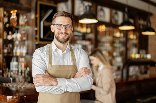 Portrait of bearded happy barista standing at a trendy coffee shop, cafe - small business concept