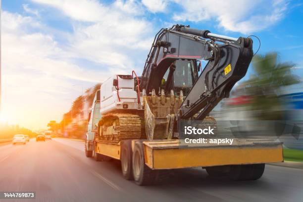 Transportation Of A Dirty Excavator On A Truck Trailer After Its Work Motion Speed And Blur Effect On City Highway During Sunset Sky Stock Photo - Download Image Now