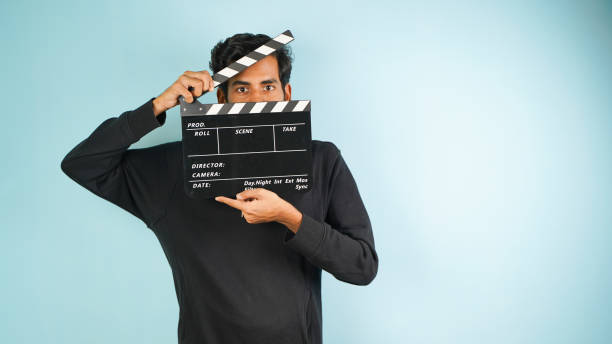 istock Young Asian Indian man standing holding clapperboard shocked, hiding behind clapper board used in film making, isolated on color background studio portrait 1444770543