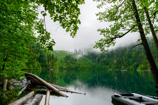 The rubber boat in the tropical forest the background of lake and green trees. The pouring tropical rain on the mountain lake.