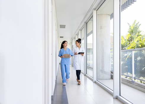 Doctor and nurse talking in the corridor of a hospital while walking - healthcare and medicine concepts