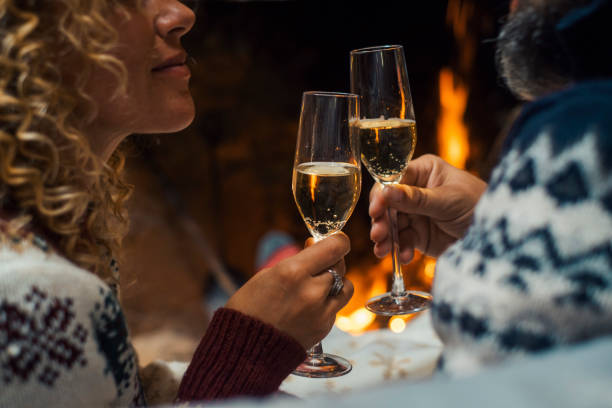 Side close up view of romantic couple celebrating together drinking champagne wine flutes in love and relationship. People man and woman celebrate new year eve in front of a fireplace holiday vacation stock photo
