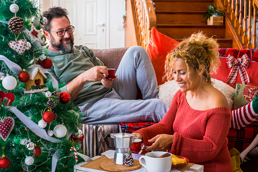 Happy couple family man and woman enjoy christmas holiday morning at home having breakfast together. Xmas tree and coffee time. December event season. Mature lady and husband enjoy indoor leisure