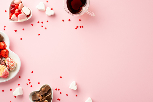 Valentine's Day celebration concept. Top view photo of heart shaped plates with sweets chocolate jelly candies and glass cup of beverage on isolated pastel pink background with copyspace